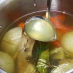 Homemade chicken stock ingredients in a stockpot with a ladle
