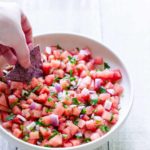 Watermelon salsa in bowl with hand dipping a corn chip