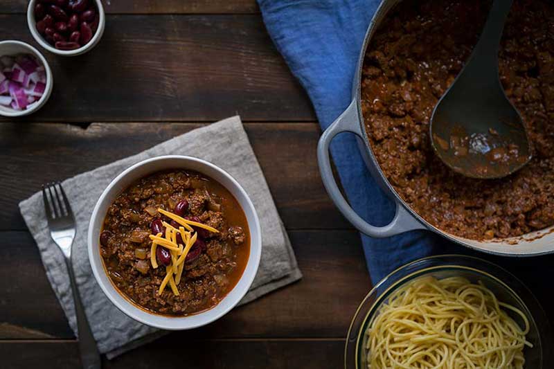 Cincinnati chili in a bowl, topped with garnishes. 