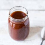 Sweet and Tangy BBQ Sauce in a mason jar on a pale backdrop.