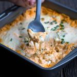 Buffalo chicken dip being scooped with a spoon. Oozing cheese dripping back into the pan.