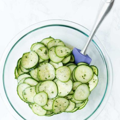 Close up shot of cucumber salad in a large bowl with a spatula.
