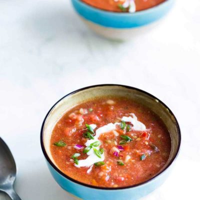Tomato gazpacho soup in a blue bowl on a white backdrop.