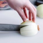 How To Chop An Onion Tutorial showing a hand pressing an onion halve onto a cutting board while a knife makes a slice