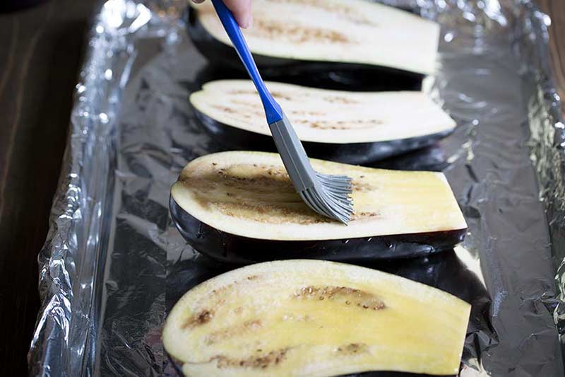 brushing olive oil onto eggplant that's been sliced in half.