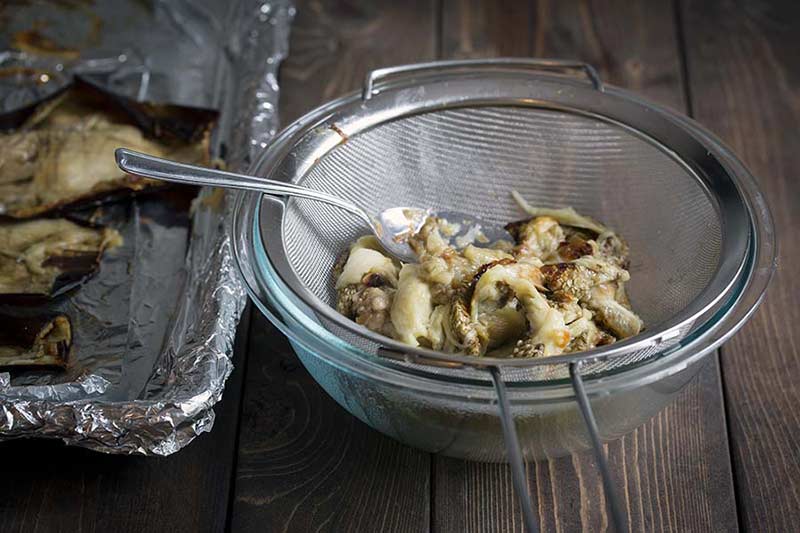 Eggplant pulp in a mesh strainer set over a bowl