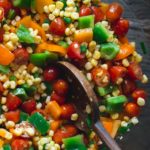 Corn salad in a grey bowl surrounded by bell peppers and tomatoes