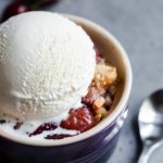 Cherry crisp in a small bowl topped with a scoop of vanilla ice cream