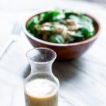 Finished tahini dressing recipe in a glass bottle with salad in the background