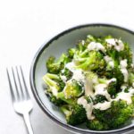 bowl of broccoli with cheese sauce next to a fork