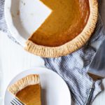 Overhead photo of pumpkin pie from scratch in a pie dish next to a slice of pumpkin pie