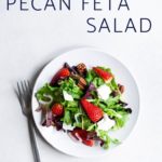 Mixed greens salad with strawberries, pecans and feta on a plate with a fork.