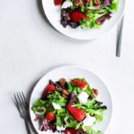 Mixed greens salad with strawberries, pecans and feta on a plate with a fork.