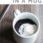 Mug brownie topped with whipped cream next to a spoon