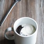 brownie in a mug topped with whipped cream next to a spoon