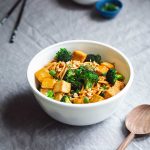 Spicy noodles with tofu and broccoli in a serving bowl next to a wood spoon.